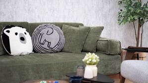 A green sofa with two decorative pillows, a small table with a bowl of colorful items, and a plant in the corner. - The Peak Tengachaya (Osaka)