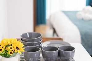 A table with grey cups and saucers, a white vase with yellow flowers, and a blue bed in the background. - The Peak Tengachaya (Osaka)