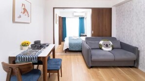 A modern room with a sofa, a dining table with chairs, a bed with a blue bedspread, and a wall-mounted air conditioner. - The Peak Tengachaya (Osaka)