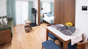 A room with a bed, a TV, a dining table set with plates and bowls, a sofa, and a small cart. - The Peak Tengachaya (Osaka)