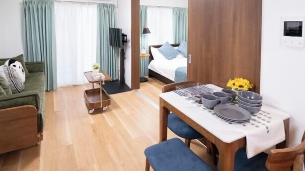 A room with a bed, a TV, a dining table set with plates and bowls, a sofa, and a small cart. - The Peak Tengachaya (Osaka)