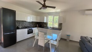 A modern kitchen with white cabinets, a black refrigerator, a glass dining table, and a ceiling fan. - Casa Alfarobeira, vila for 4P+baby with private pool in natural protect erea (São Bartolomeu de Messines)