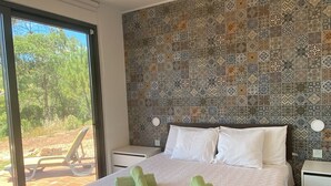 A modern bedroom with a large bed, a ceiling fan, a patterned wall, and a view of the outdoors. - Casa Alfarobeira, vila for 4P+baby with private pool in natural protect erea (São Bartolomeu de Messines)