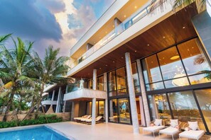 Een modern hotel met een groot zwembad, meerdere balkons en palmbomen.