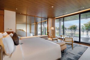 Een moderne hotelkamer met een groot bed, een zithoek met een tafel en stoelen, en uitzicht op palmbomen door grote ramen.