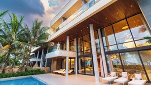 Un edificio moderno a più piani con ampie finestre, una zona piscina con lettini e palme.