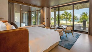 Una moderna camera d'hotel con un grande letto, un'area salotto con un tavolo e vista sulla spiaggia.