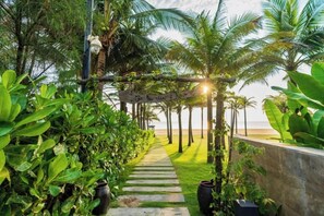 A pathway lined with lush greenery and palm trees leading to a beach. - All Inclusive Luxury: Private Beachfront Paradise (Da Nang)