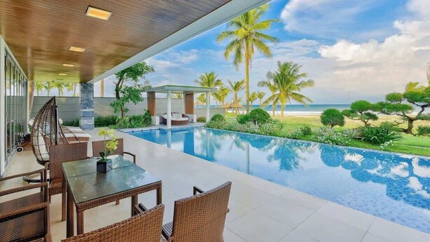 A pool area with a view of the beach, outdoor furniture, and a covered seating area. - Luxe 6BR Beachfront Villa: Group Getaway Haven (Da Nang)