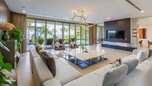 A modern living room with a large TV, comfortable seating, and a view of the ocean. - Luxe 6BR Beachfront Villa: Group Getaway Haven (Da Nang)