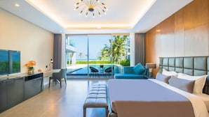 Una habitación de hotel moderna con una cama grande, un escritorio con televisor, un comedor con vista al océano y un balcón con palmeras.