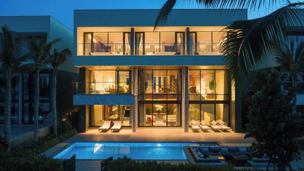 Una casa moderna de dos pisos con piscina al frente, amplias ventanas de vidrio y zonas de estar exteriores.