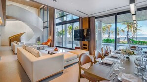 Una habitación de hotel moderna con una escalera de caracol, un comedor con vista al océano y un televisor de pantalla plana grande.