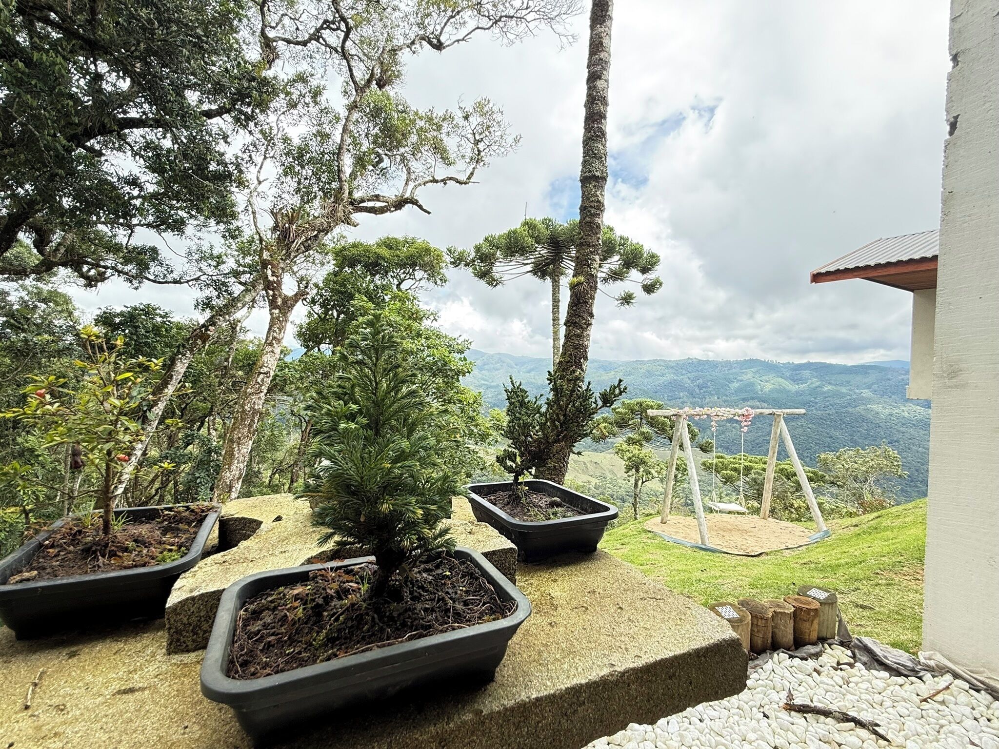 A garden with potted plants and a swing set overlooking a mountainous landscape.