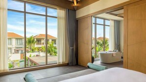 A modern hotel room with a large bed, a bathtub, and a view of the resort's pool and buildings.
