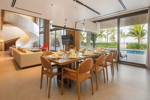 A modern dining area with a long table set for six, a sofa, and a TV.