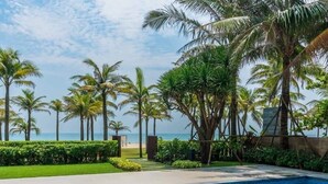 A poolside scene with a person relaxing, a tray of food and drinks, and a view of the ocean and palm trees. - Elegant Retreat for Discerning Travelers (Da Nang)