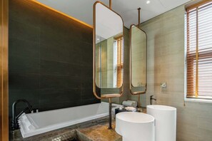 A modern bathroom with a bathtub, two sinks, and a large mirror.