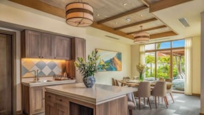 A modern kitchen with wooden cabinets, a central island, pendant lighting, and a dining area with a view of greenery. - Luxe 5 Star Villa Private Pool Resort Access (Da Nang)