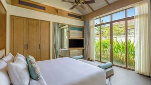 A bedroom with a large bed, a ceiling fan, a TV, and a sliding glass door leading to a garden. - Luxe 5BR Villa: Beachfront Breakfast Pool (Da Nang)