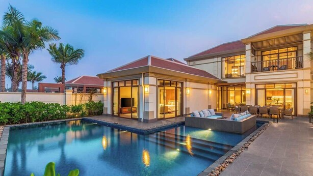 A modern resort with a swimming pool, outdoor seating, and a well-lit building facade. - Luxe 5BR Villa: Beachfront Breakfast Pool (Da Nang)
