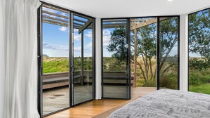 Une chambre dotée d’une grande porte-fenêtre coulissante qui donne sur un espace extérieur offrant une vue sur les arbres et un paysage verdoyant.