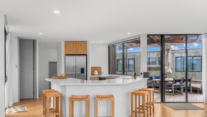 Une cuisine moderne avec un îlot central, des tabourets en bois et un grand réfrigérateur.