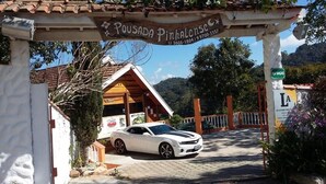 A white car parked under a sign that reads "Pousada Pinhalense." - Pousada Pinhalense (Santo Antonio do Pinhal)