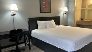 A hotel room with a large bed, a desk, two wall-mounted lamps, and a framed artwork above the bed. - Suni's Place (Union City)