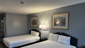 A hotel room with two single beds, a nightstand with a lamp, and two framed pictures on the wall. - Suni's Place (Union City)