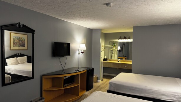 A hotel room with two beds, a TV, a lamp, a mirror, a painting, and a wooden shelf. - Suni's Place (Union City)