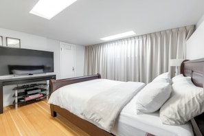 A hotel room with a bed, a TV, a desk with a computer, and a window with curtains.