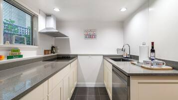 Een moderne keuken met witte kasten, een roestvrijstalen spoelbak en een raam met jaloezieën.