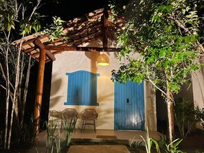 Een rustieke buitenruimte met een houten pergola, twee blauwe deuren en een hanglamp.