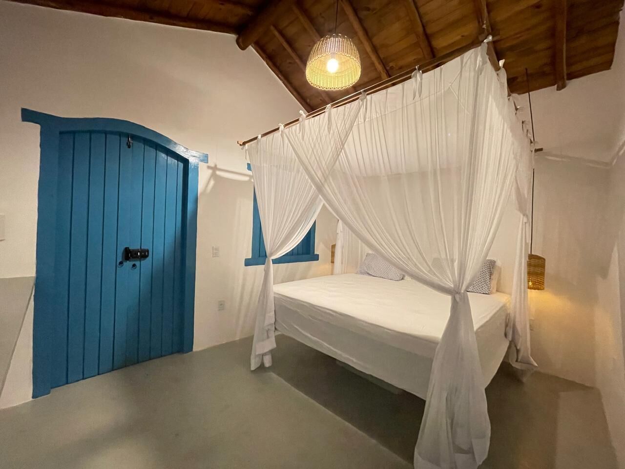 Una camera da letto con un letto sotto una tenda bianca, una porta blu e un soffitto in legno.