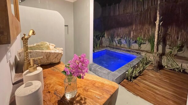 A bathroom with a stone sink, a toilet paper holder, and a vase with flowers. There is a pool with a wooden deck and plants around it. - Trancoso Biriba guest house (Porto Seguro)