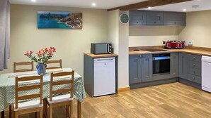 Eine kompakte Küche mit Kühlschrank, Mikrowelle und Backofen. Es gibt einen Essbereich mit Tisch und Stühlen, sowie ein Gemälde mit einer Küstenlandschaft an der Wand.