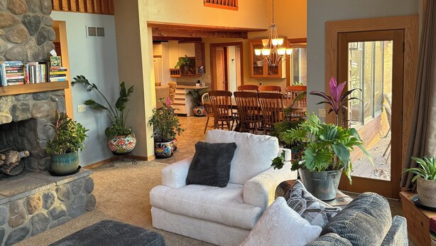 A cozy living room with a stone fireplace, a dining area with wooden furniture, and a kitchen in the background. - Ugly Duckling Lodge - Swan Lake Retreat (Dalton)