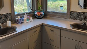 A bathroom with two sinks, a mirror, and a window with a view of trees and grass. - Ugly Duckling Lodge - Swan Lake Retreat (Dalton)