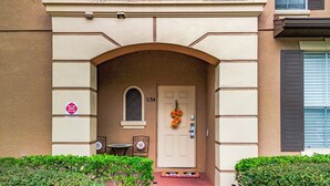 Fachada beige de un edificio, una puerta con el número 1134 y una pequeña mesa con sillas afuera.