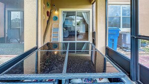 Un espacio al aire libre cubierto con piso de vidrio, baranda metálica y vista a una casa a través de una puerta de cristal.