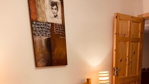 Un dormitorio con una cama, una lámpara de noche, un armario de madera y una obra de arte colgada en la pared.