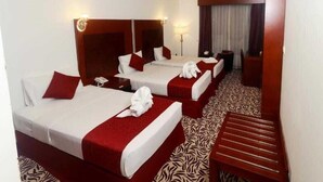 Habitación de hotel con dos camas, ropa de cama roja y blanca, alfombra con estampado de cebra, un banco de madera y un escritorio con lámpara.