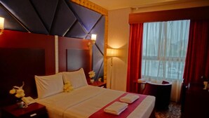 Habitación de hotel con una cama grande, una mesita de noche con lámpara, un teléfono y una ventana con cortinas rojas.