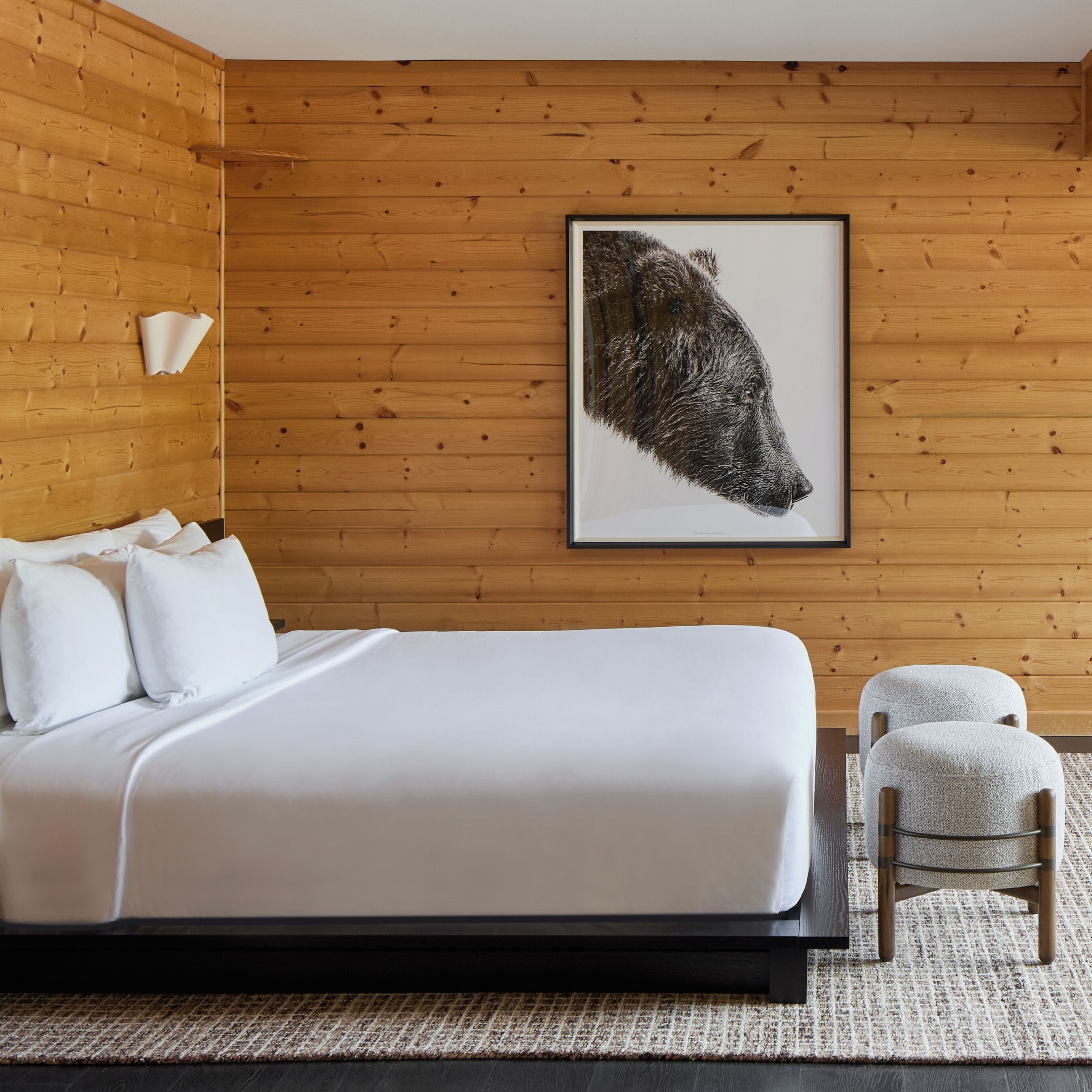 A bedroom with a large bed, a wooden wall, a framed picture, and a chair.