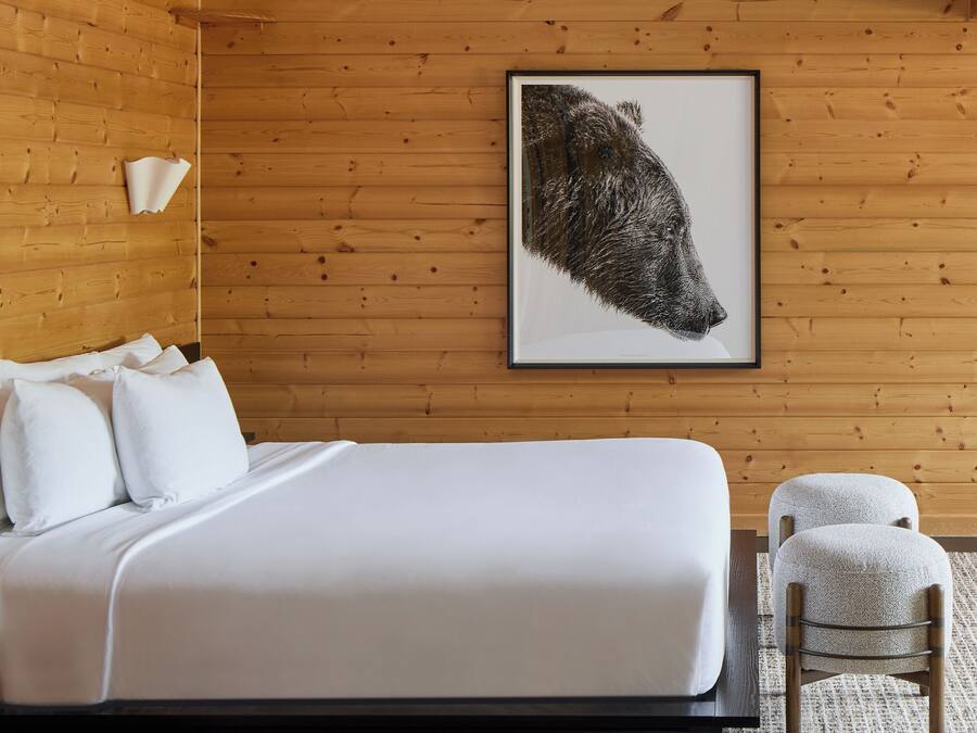 A bedroom with a large bed, a wooden wall, a framed picture, and a chair.