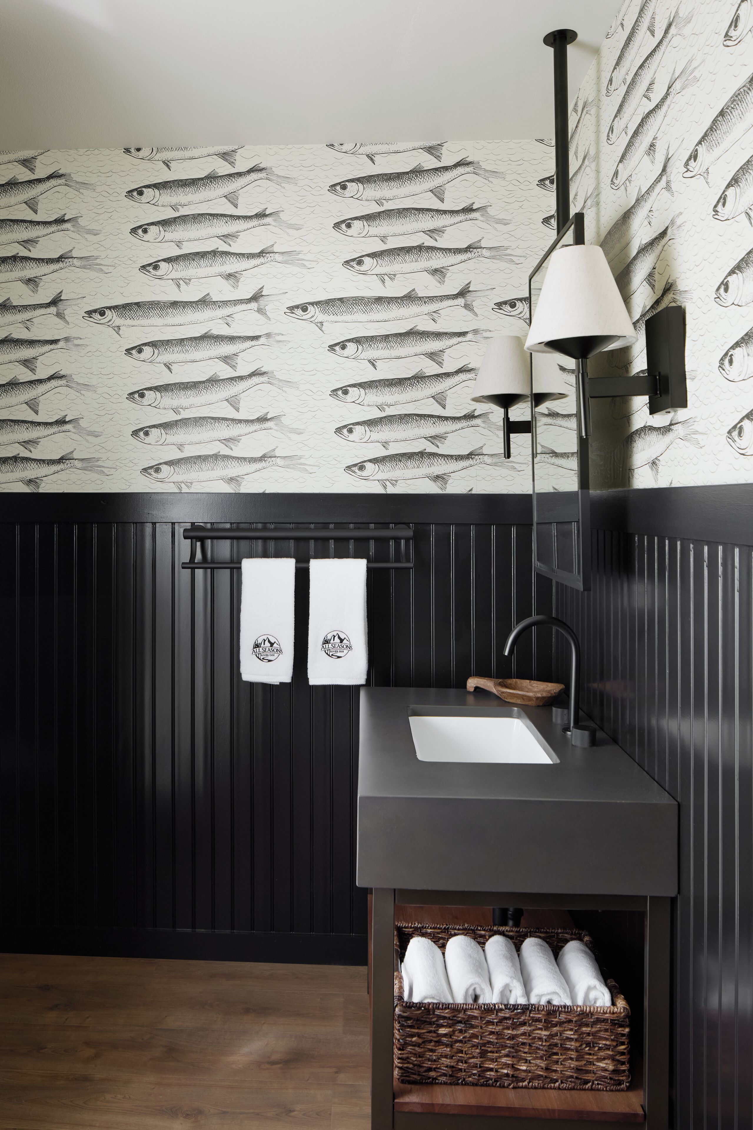 A modern bathroom with a black and white fish wallpaper, a black sink, and two towels hanging on a rack.