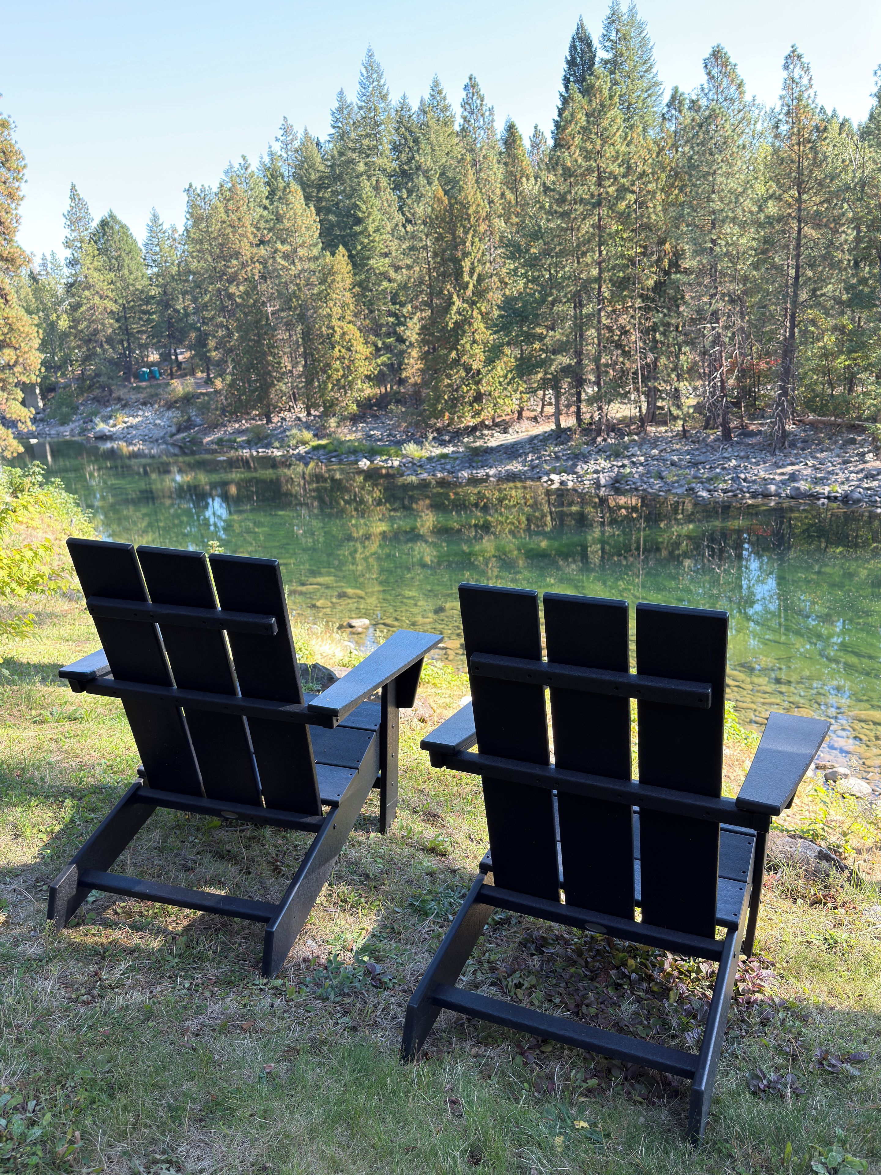 To Adirondack-stole med udsigt til en rolig sø omgivet af træer.
