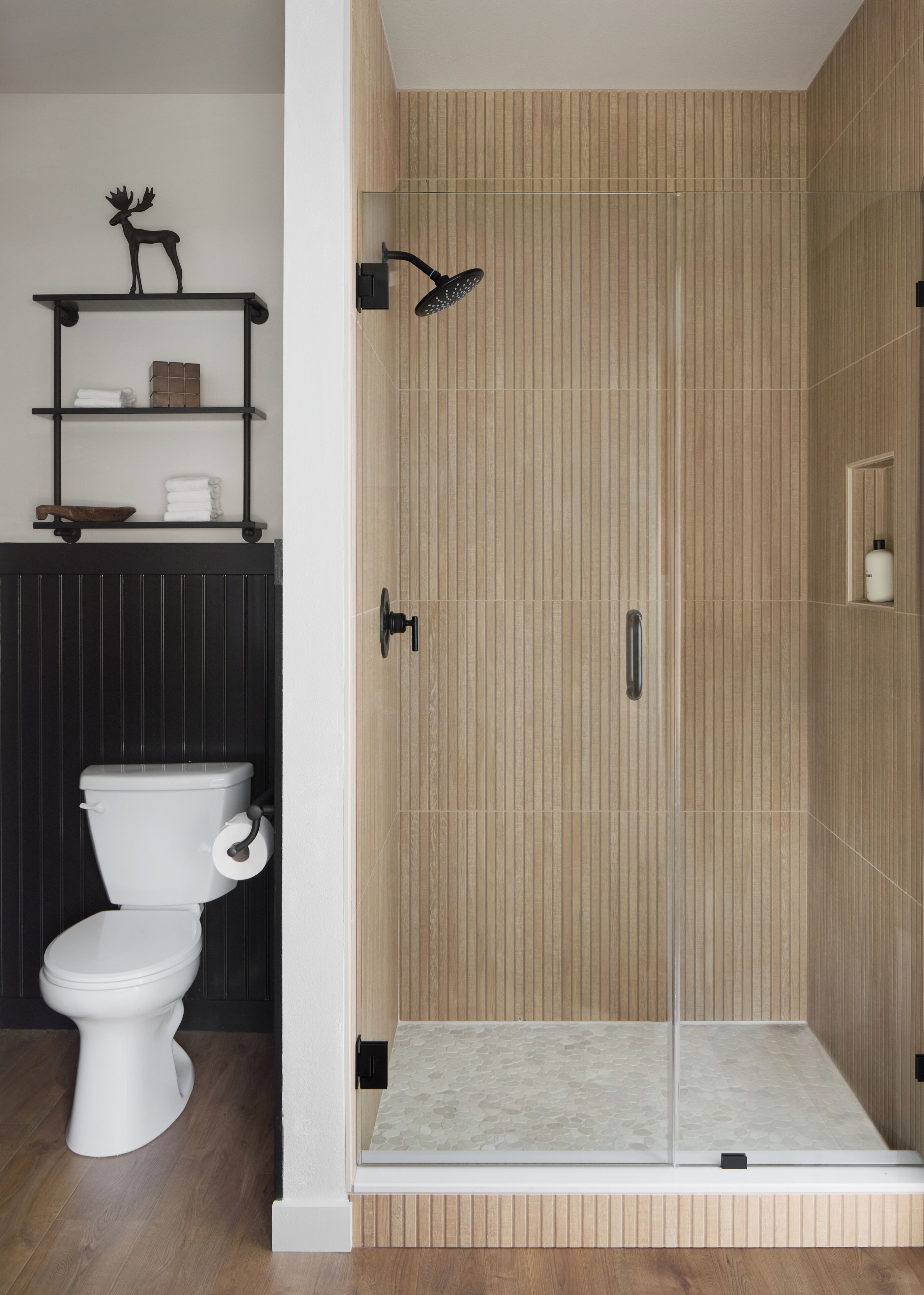 A modern bathroom with a toilet, a shower with a glass door, and shelves with toiletries.