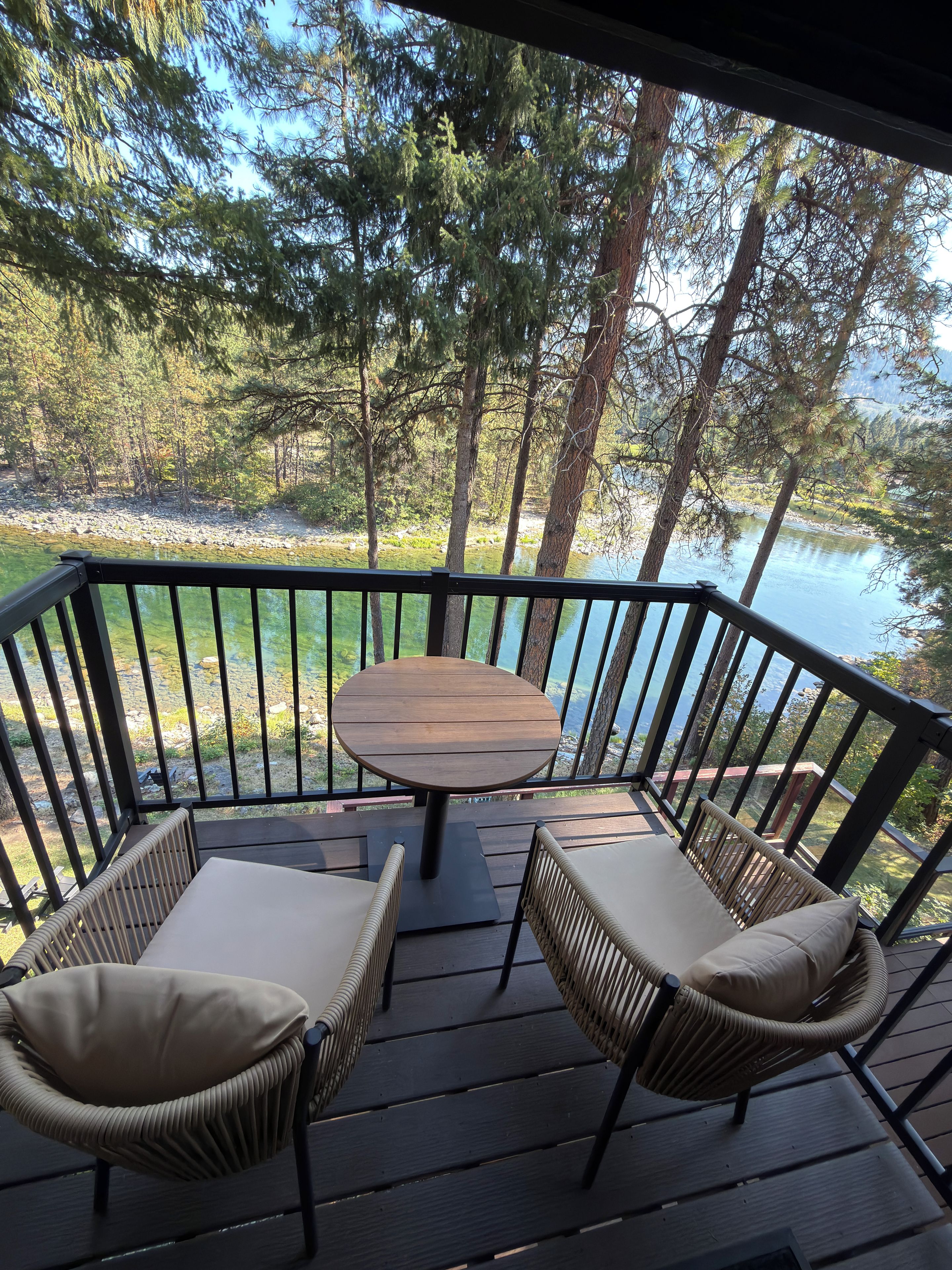 A deck with a table and two chairs, overlooking a body of water and trees.